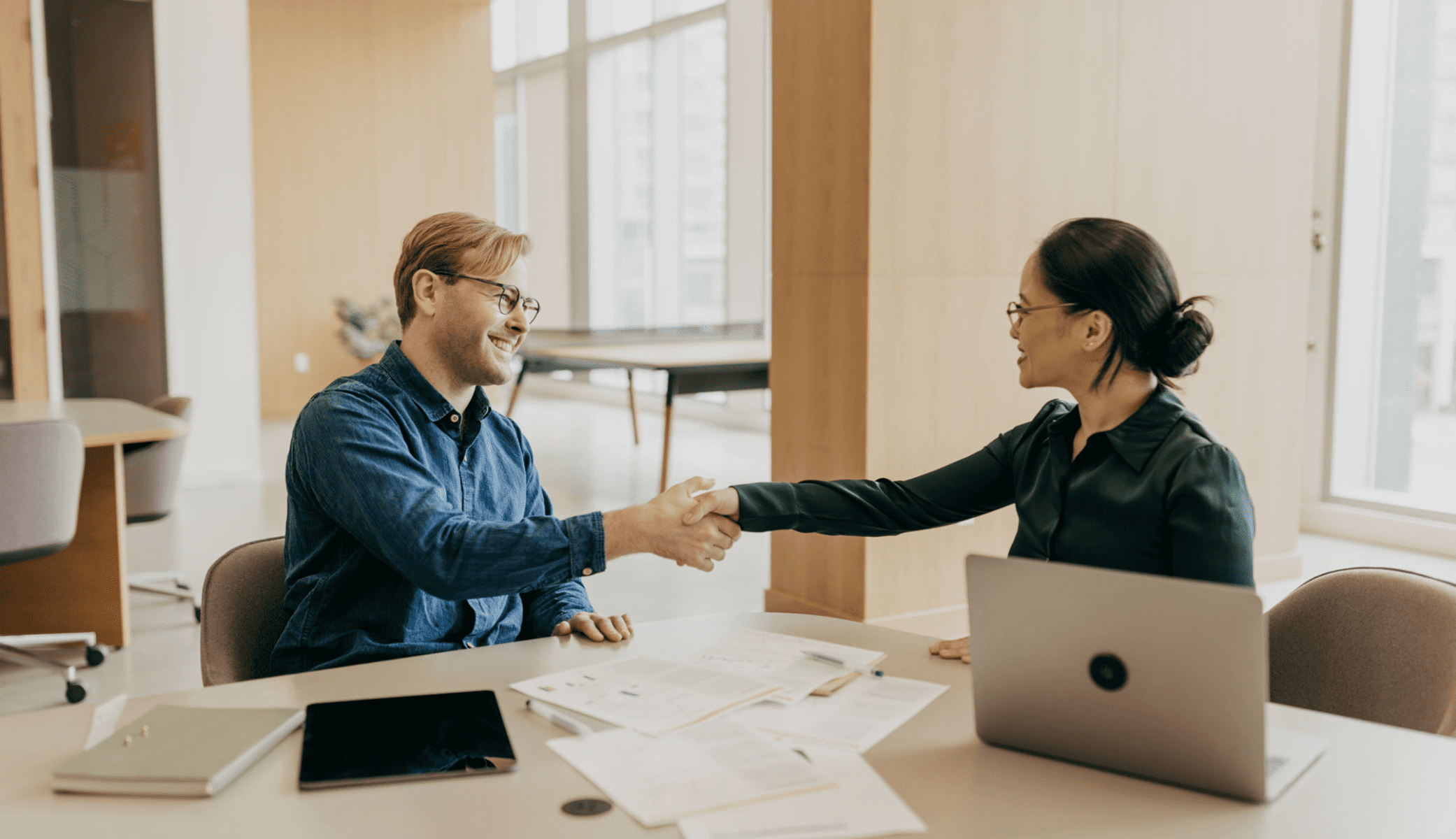 Two people shaking hands in office setting.